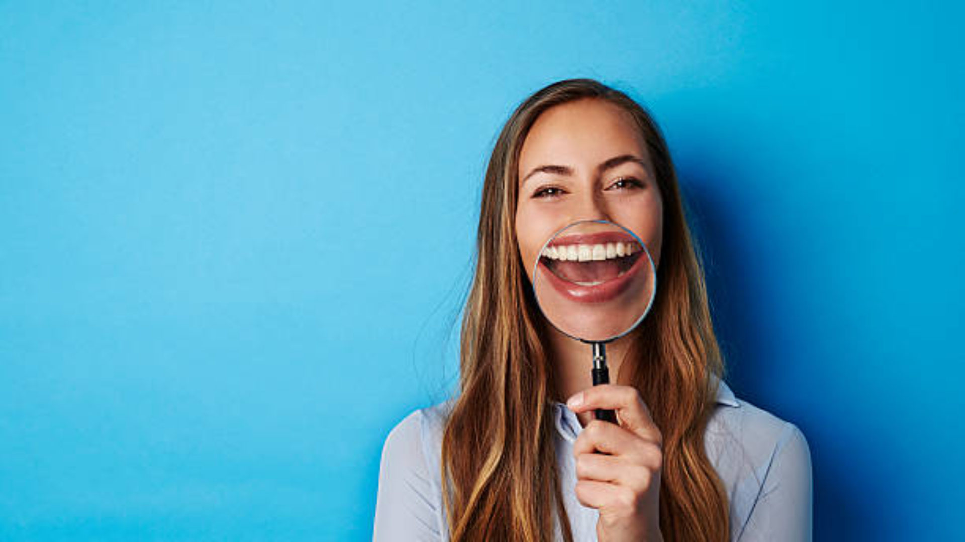 Huge smile through magnifying glass of young woman